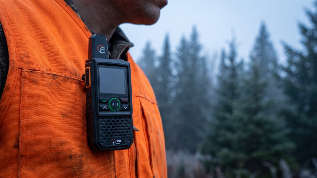 A compact Echo radio clipped to the front of a blaze-orange vest at chest height, with a misty treeline blurred behind.