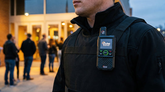 A compact handheld radio clipped to the chest strap of a security guard's vest at a venue entrance at dusk.